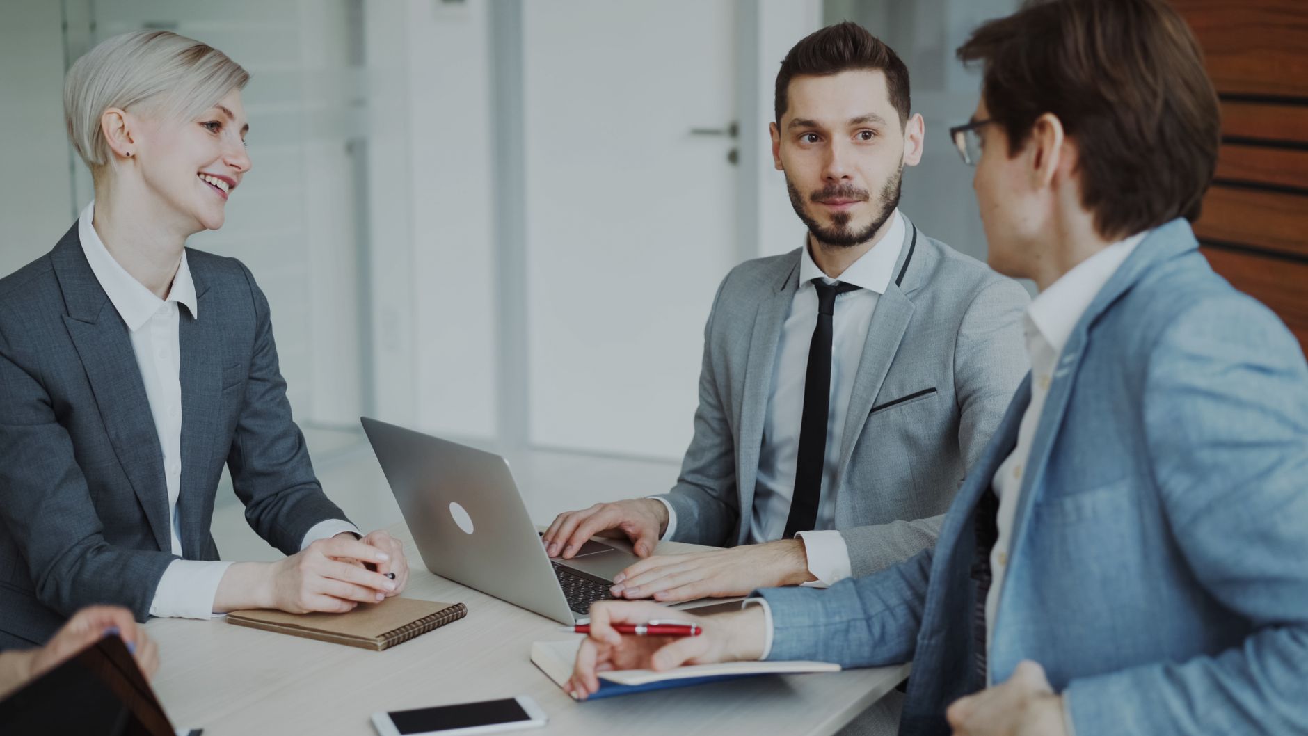 Business professionals in a meeting with laptops and notebooks, discussing strategy. — 7 Personality Traits That Help A Busin