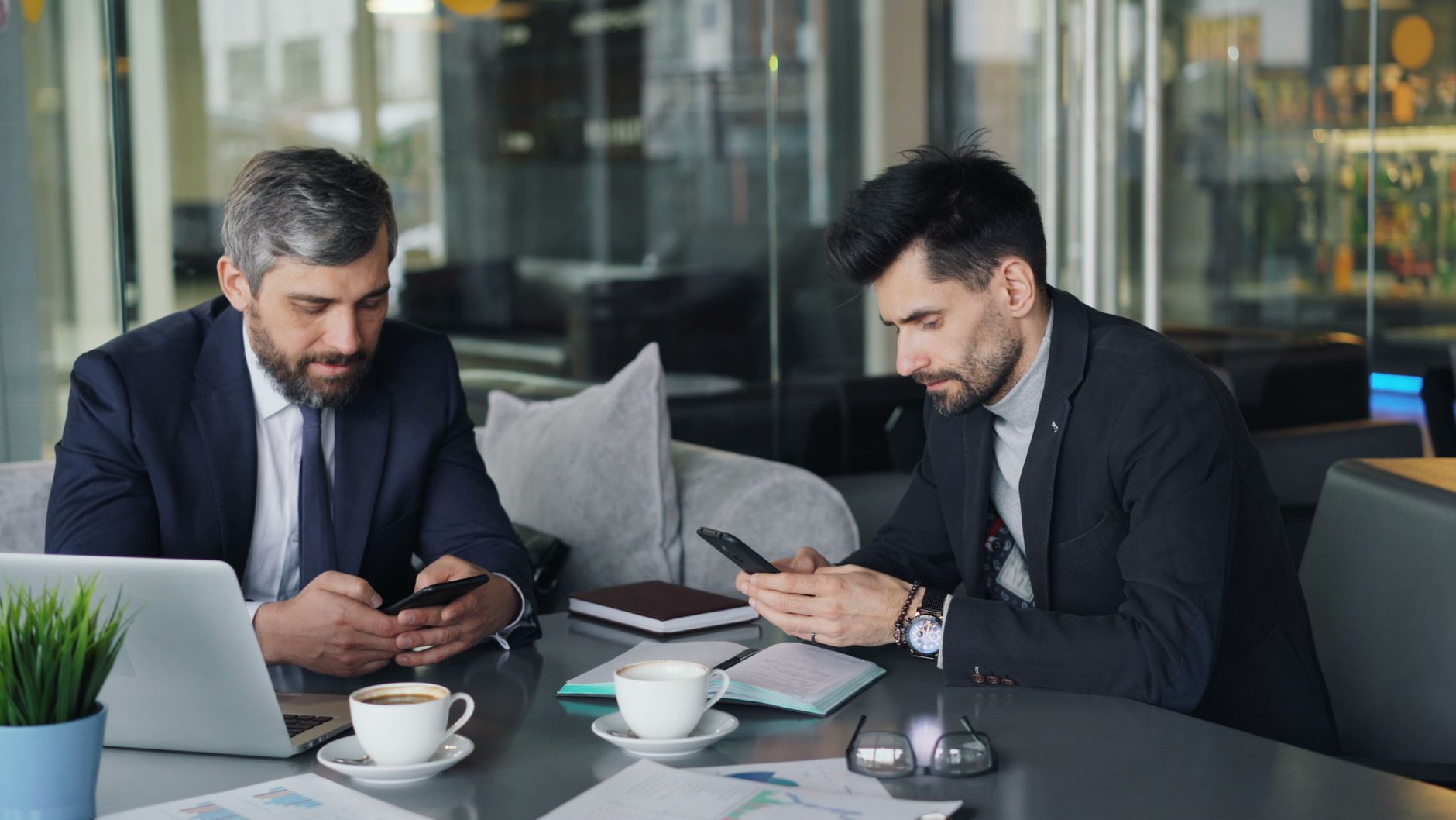 Two businessmen in a cafe working on smartphones and laptops, engaged in a meeting. — Advantages Leather Gun Holsters