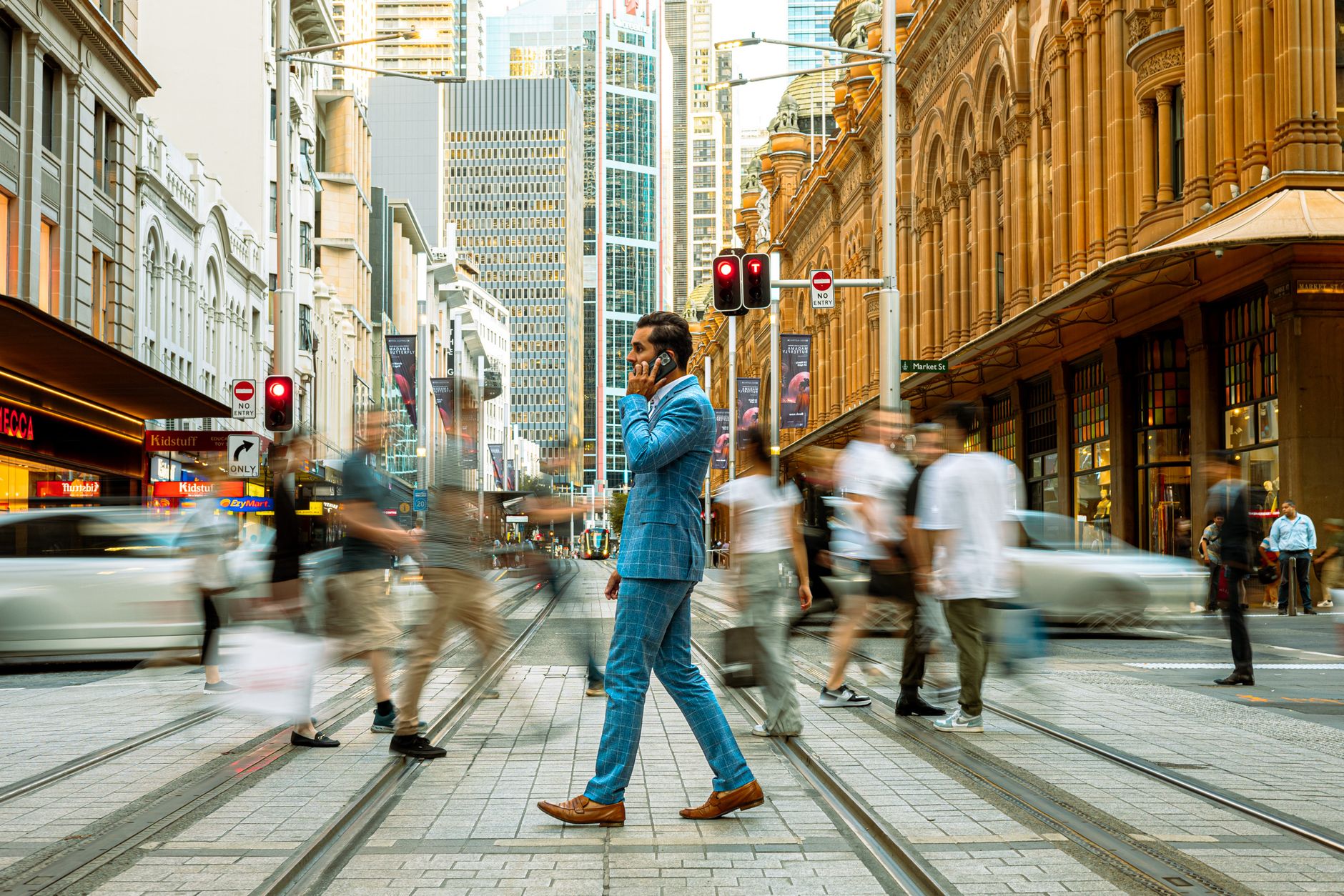A businessman in a blue suit crosses a busy street in Sydney, Australia, surrounded by motion-blurred pedestrians. — Canada's