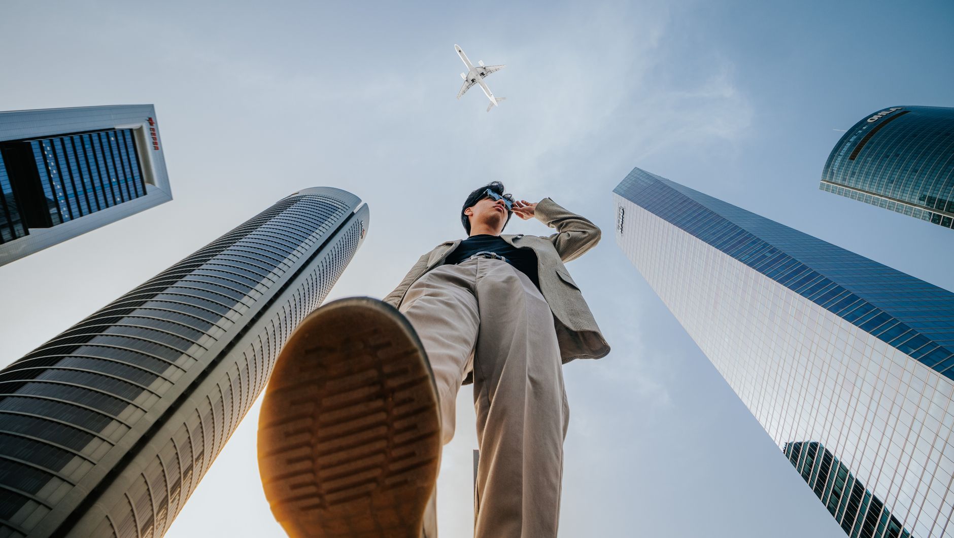 Low-angle shot of a man in a suit framed by skyscrapers and a passing airplane. — Discover Your Dream Home: New Homes in Myrt