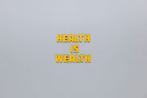 Inspirational phrase 'Health is Wealth' in bold yellow letters on a neutral gray background. — Dr. Scott Kamelle Delivering C