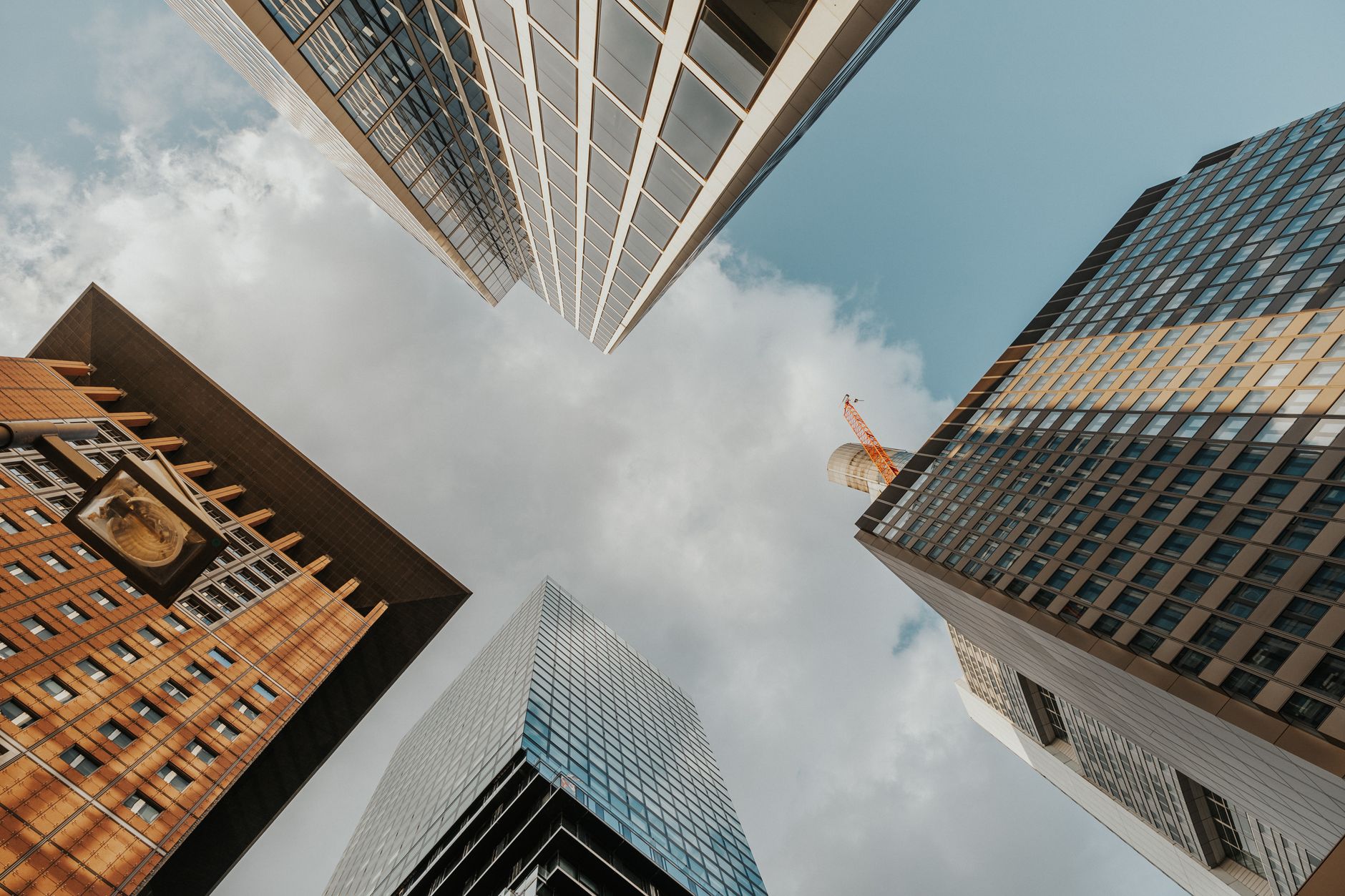 Looking up at diverse modern skyscrapers reaching into a partly cloudy sky. — Exploring insurance agency for sale opportuniti
