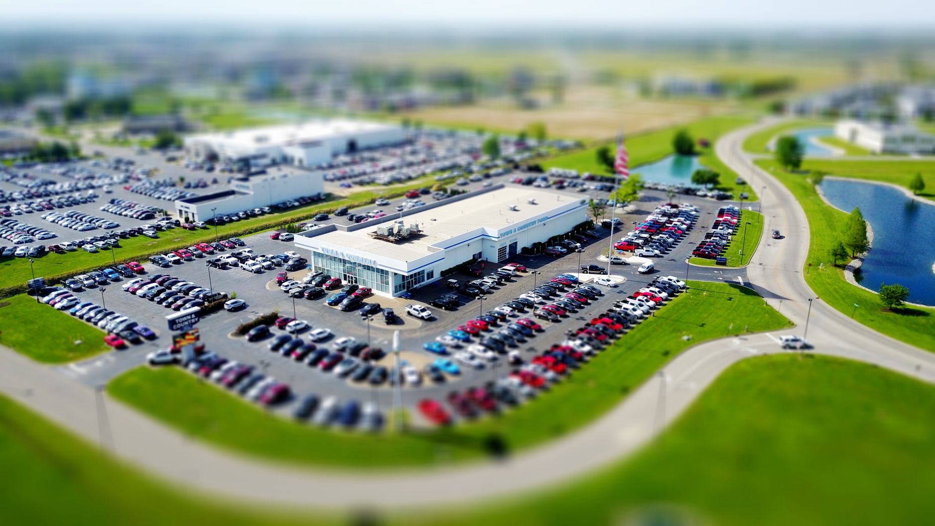 Aerial high-angle view of a bustling car dealership surrounded by parked cars in a green landscape. — How Searching for a Kar