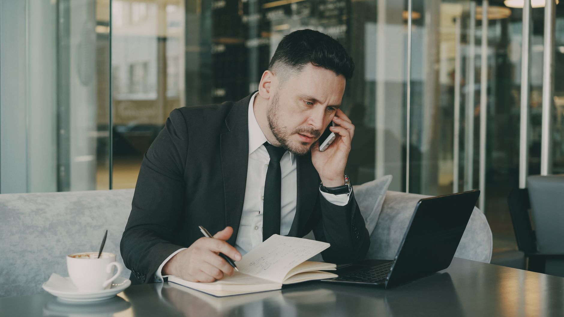 Businessman talks on phone while writing notes in a modern cafe. — What to Look for in an SEO Service Provider