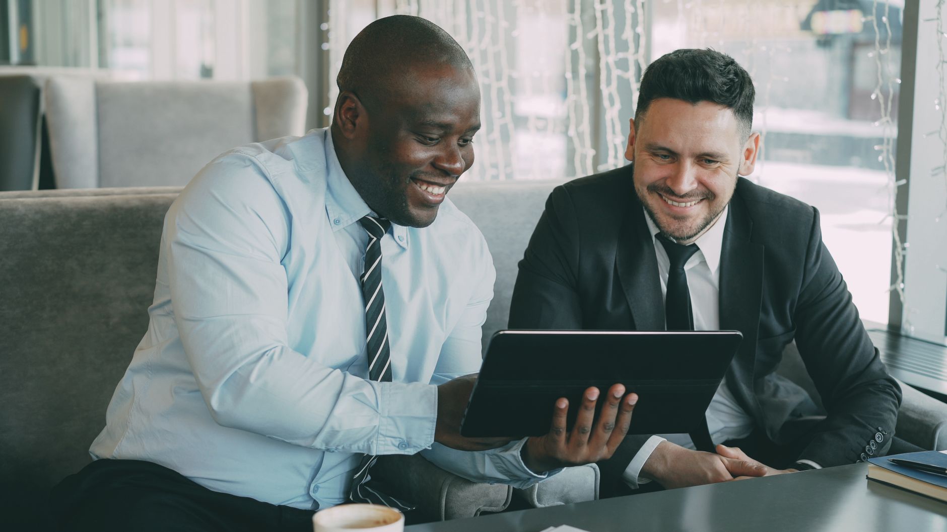 Two businessmen happily collaborating on a digital tablet in a modern cafe setting. — Your key to financial prosperity is a h